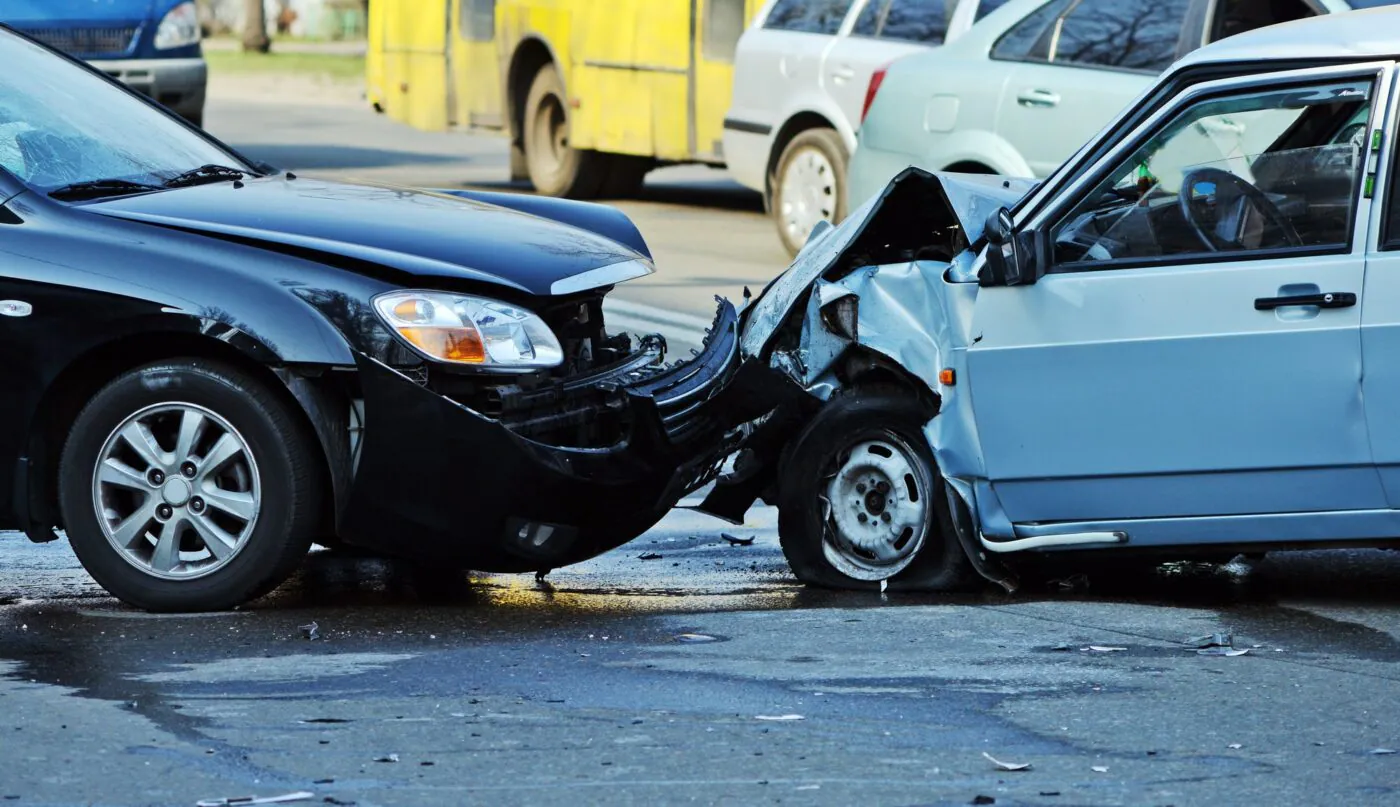 A black car and a light blue car crumpled together after a collision on a city street