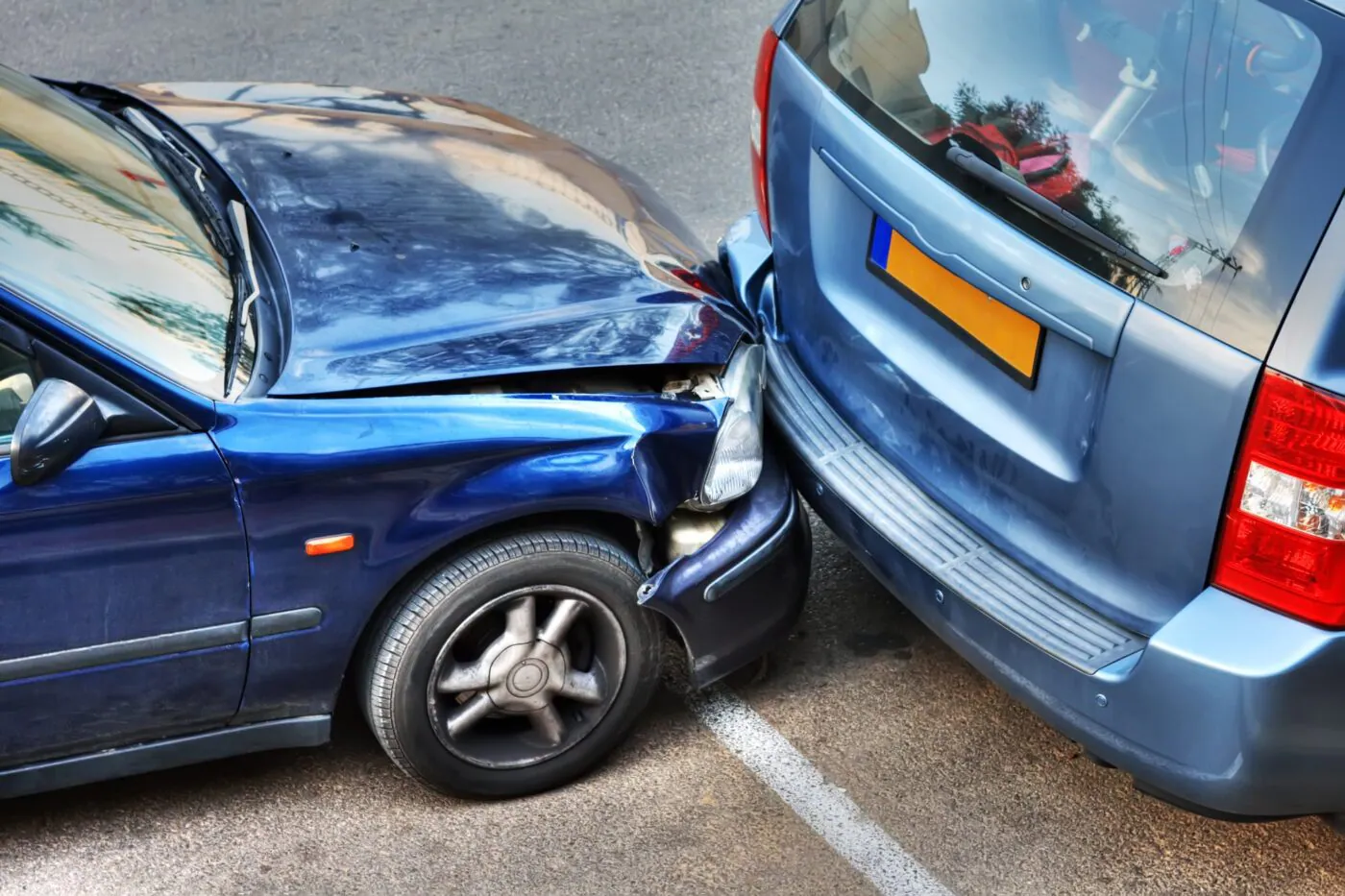 A blue car with a crumpled hood pressed into the back of a gray minivan
