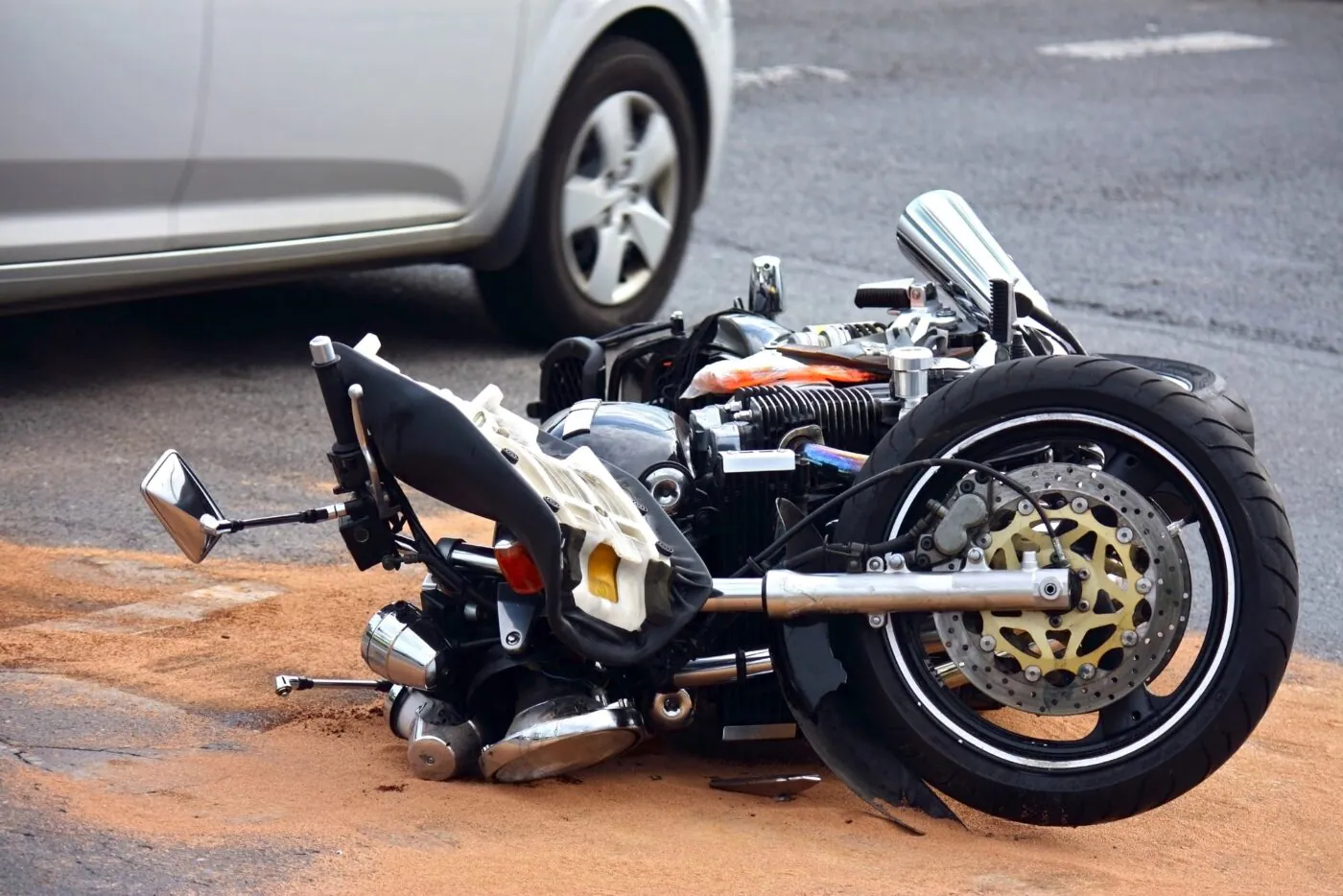 A wrecked motorcycle lying on its side in the road beside a car