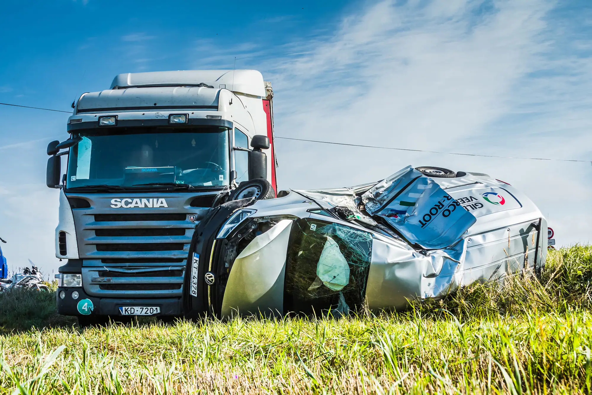 A white semi truck stopped beside a crushed silver car on a grassy roadside