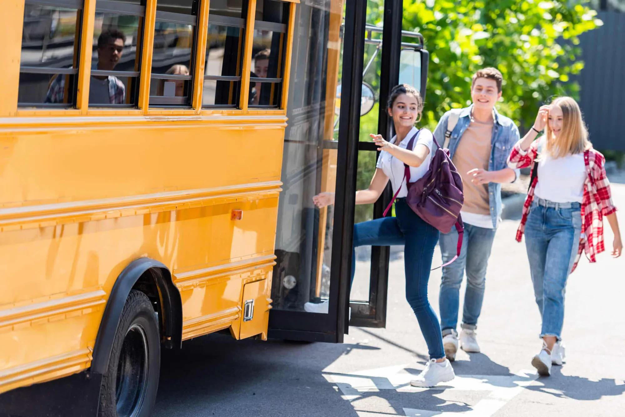 Teenage students climbing the steps of a yellow school bus