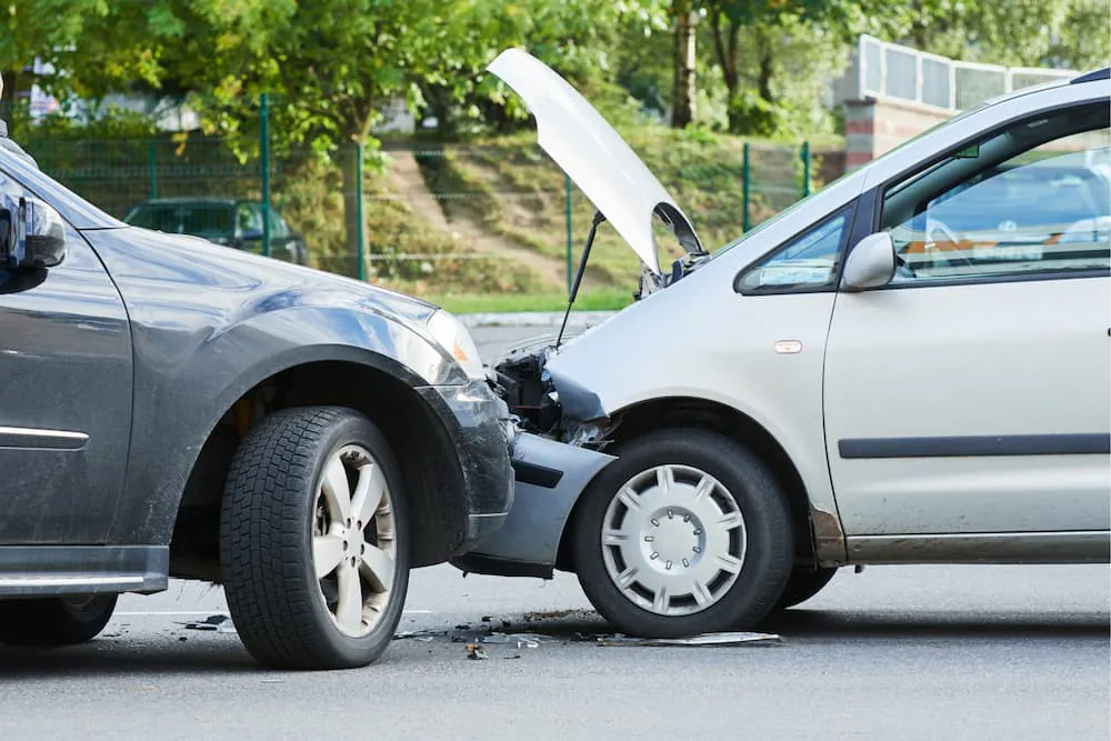 Two cars with damaged front ends after a collision on a tree-lined road