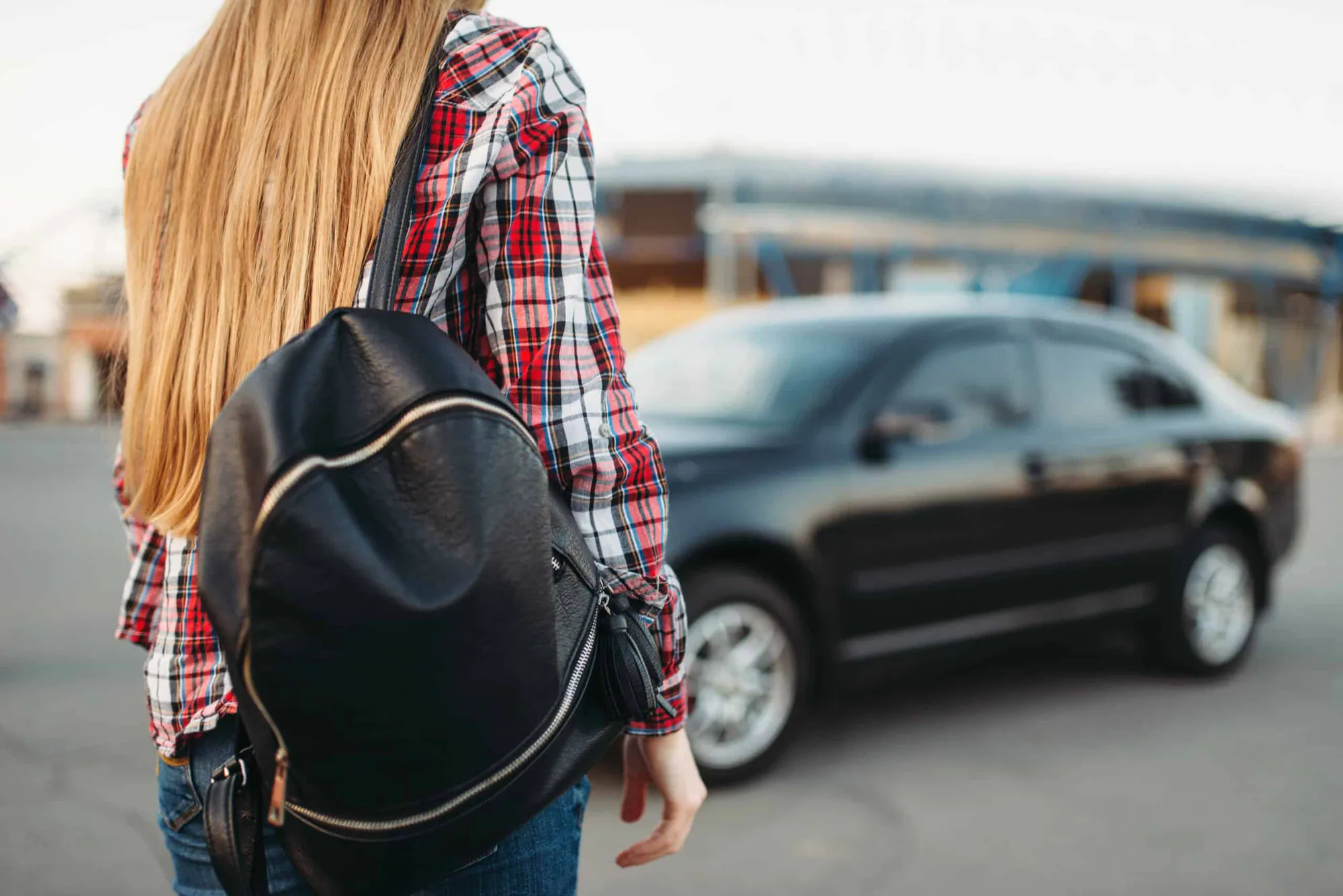 A student with a backpack stands near a parked car in a parking lot