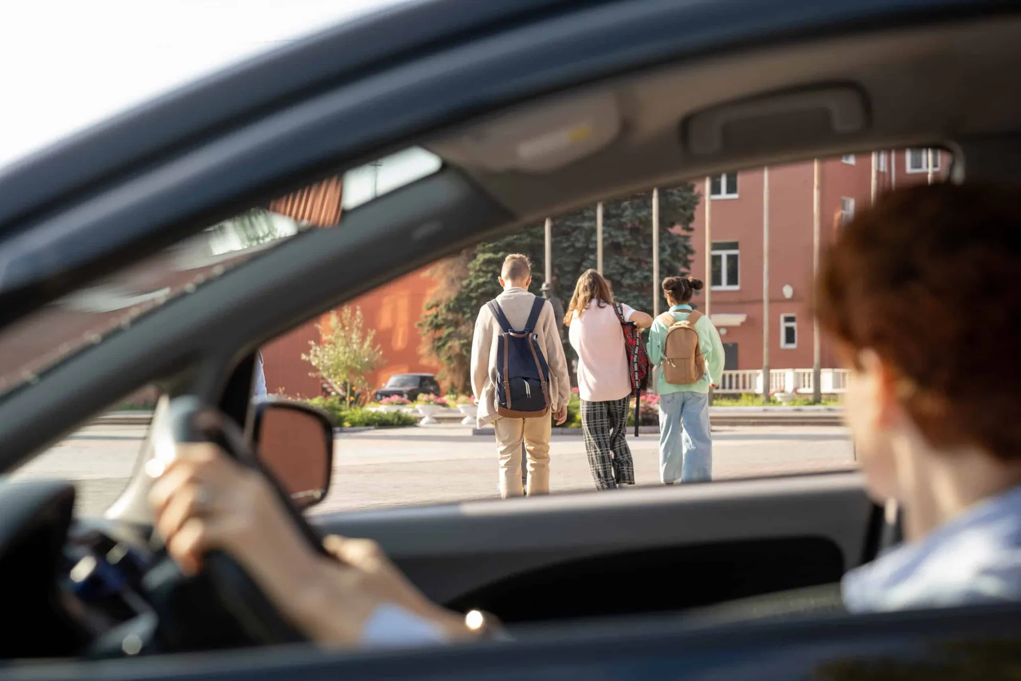 A driver waits while three people with backpacks walk across the road in front of the car