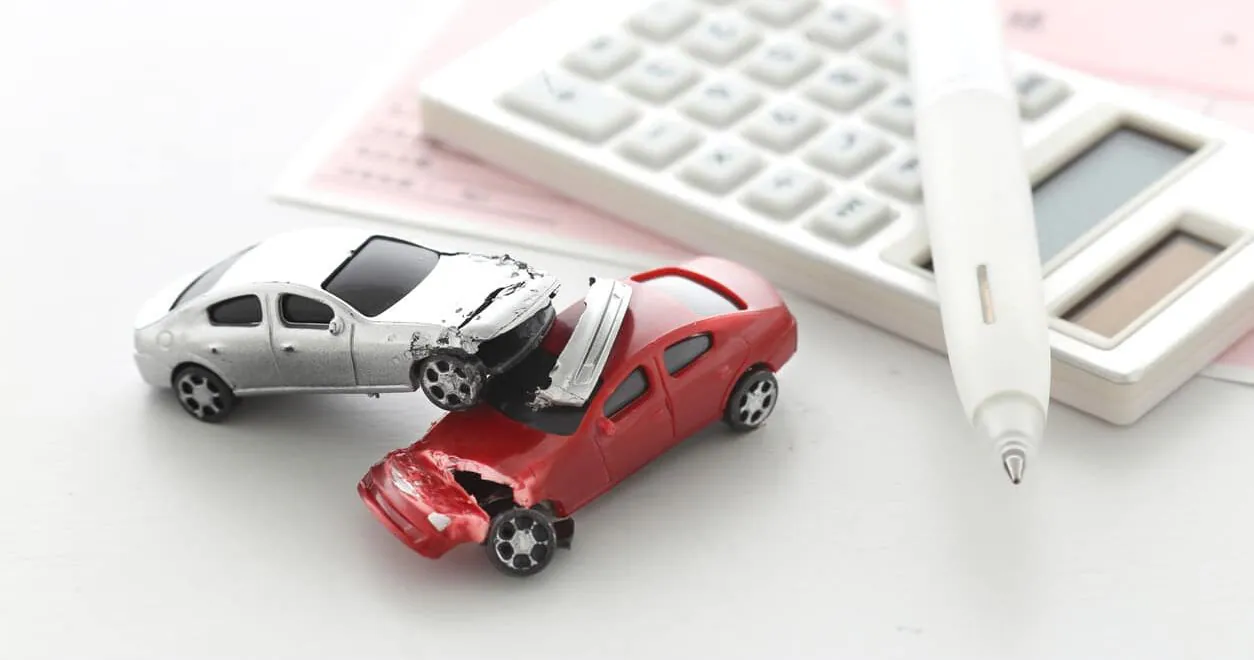 Two toy cars crashed together beside a calculator and a pen