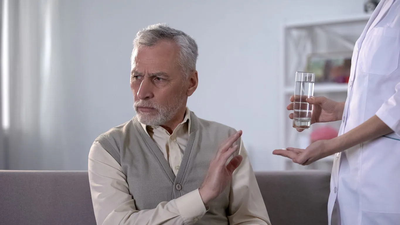 A man waves away the pills and glass of water a nurse offers him