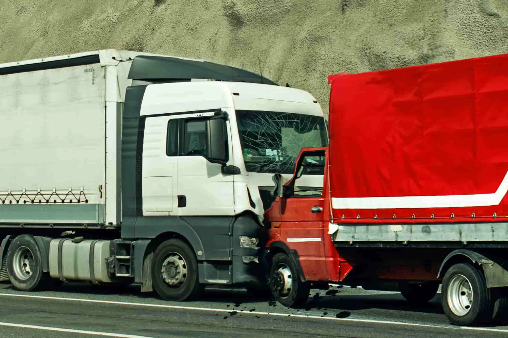 A tractor-trailer and a red box truck locked together after a collision on a highway