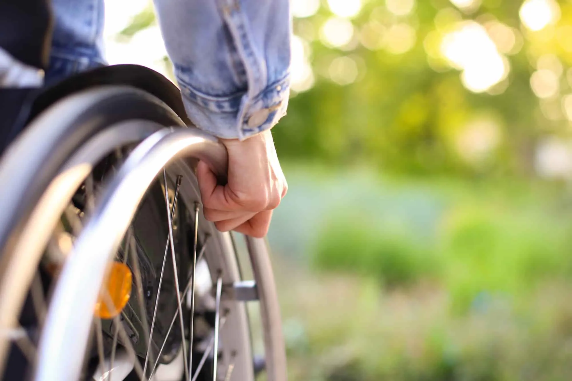 A hand on the wheel of a wheelchair, outdoors