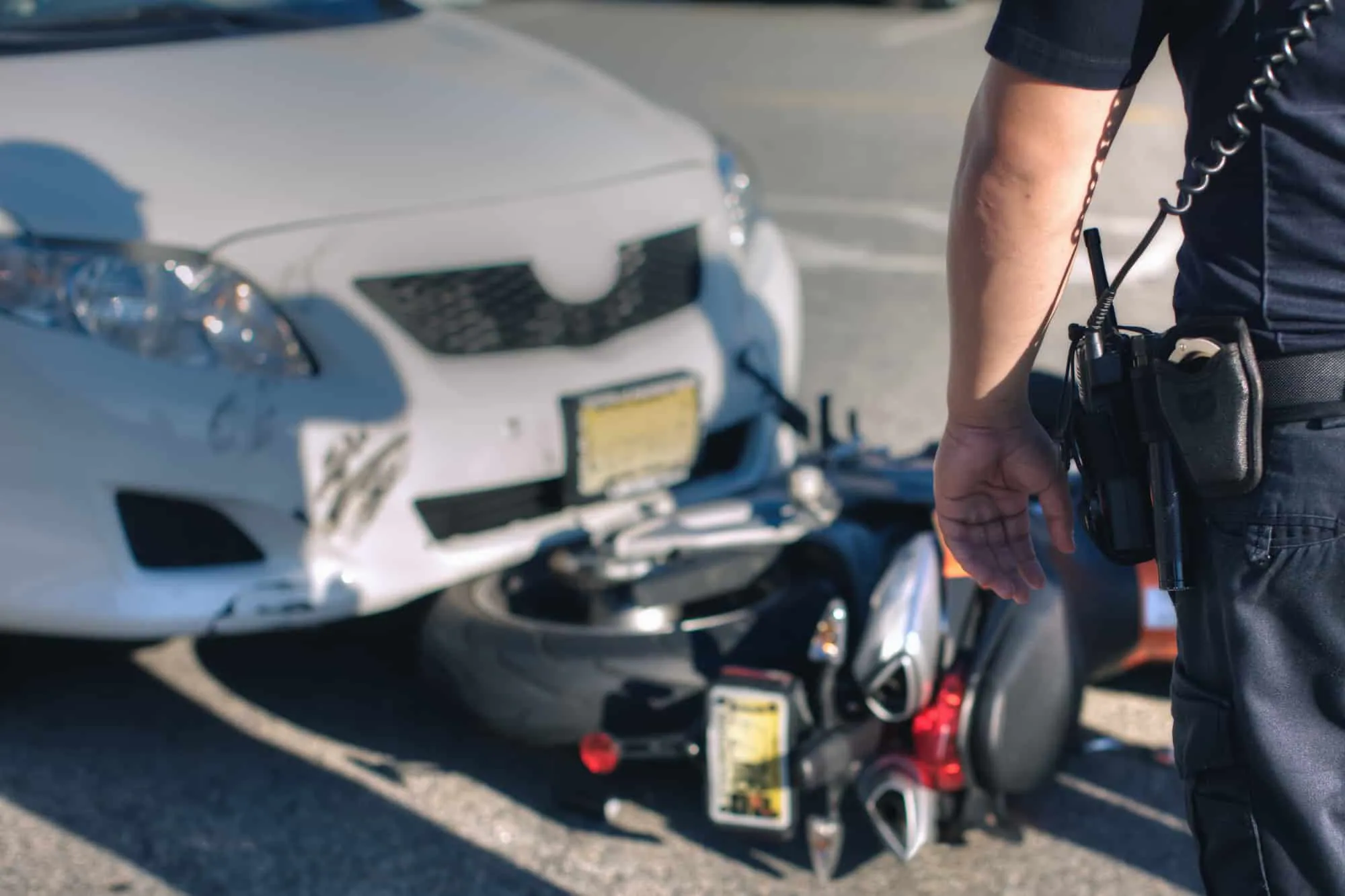 A police officer stands beside a motorcycle pinned under the front of a car