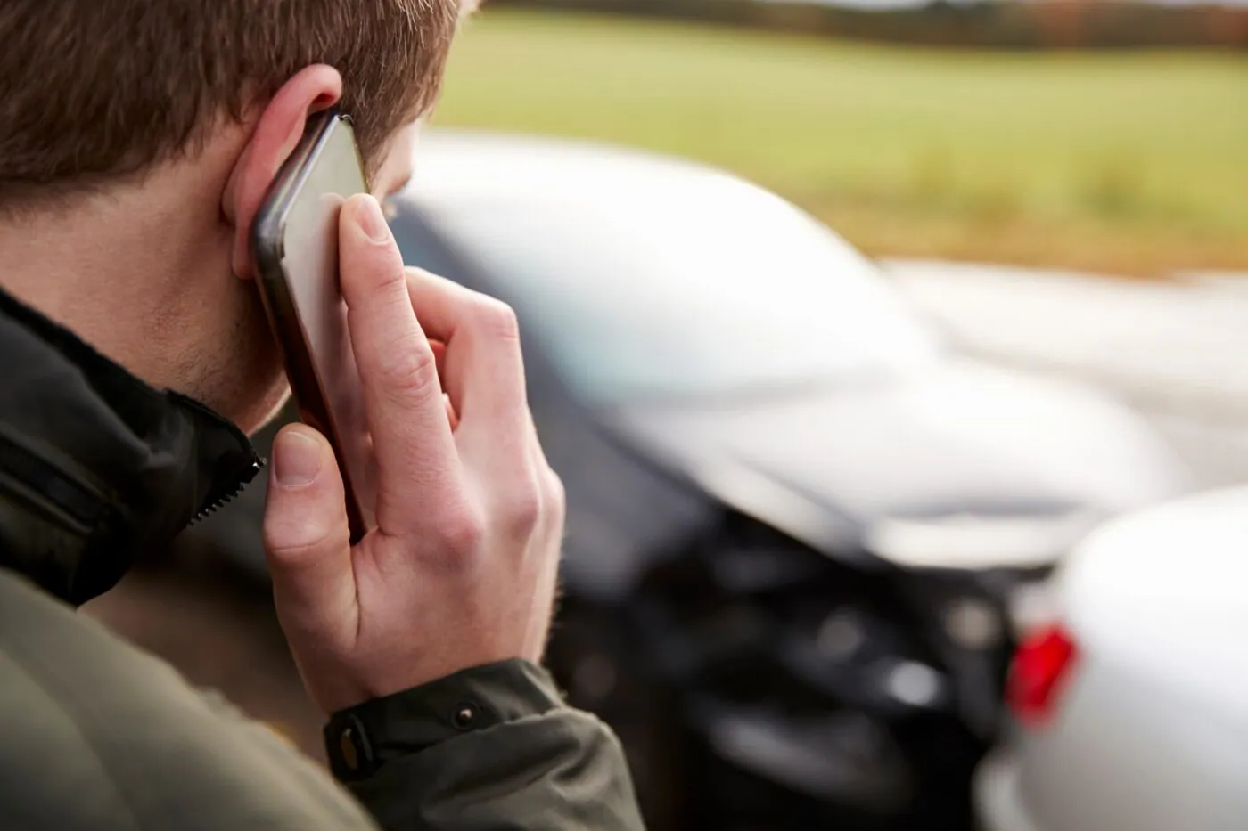 A man on the phone beside two damaged cars after a collision