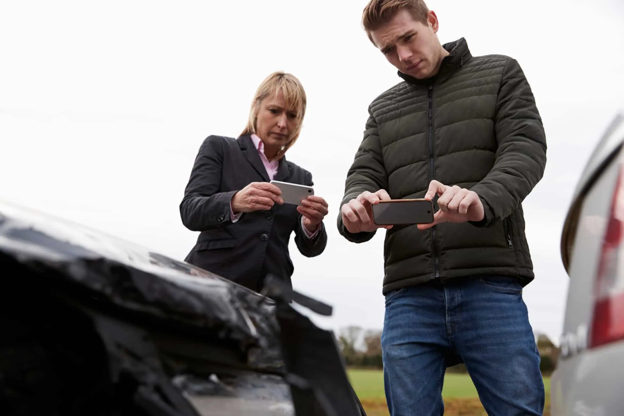 Two people photograph the damage to a car after a crash