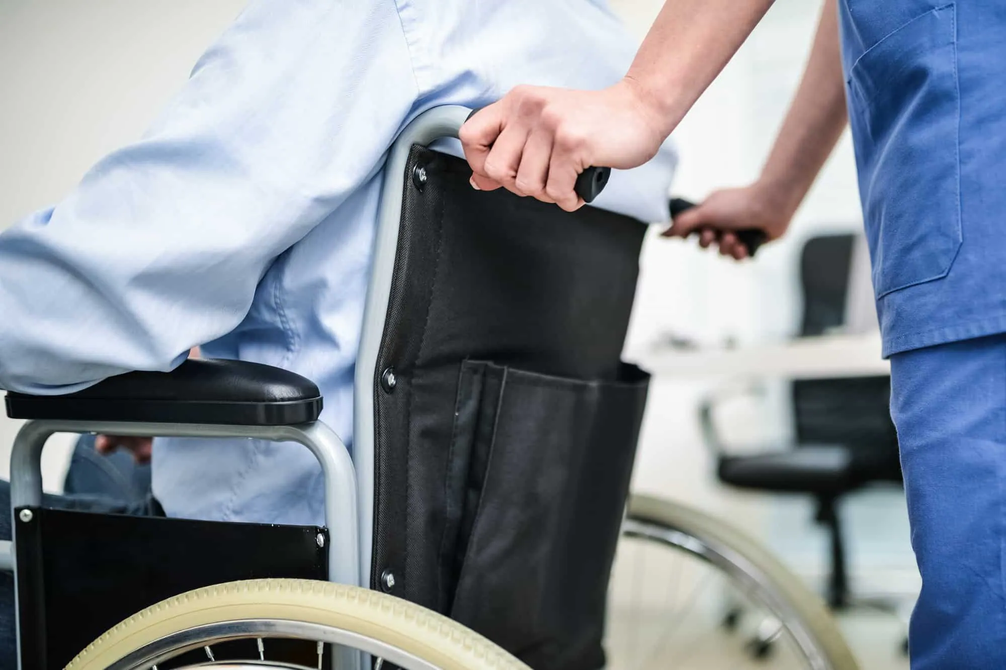 A caregiver in scrubs pushes a man in a wheelchair