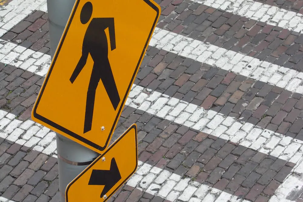 A pedestrian crossing sign beside a brick crosswalk
