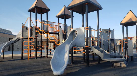 A playground with slides, climbing frames and roofed towers under a clear sky