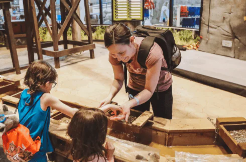 A woman and two young children playing at an indoor sand table