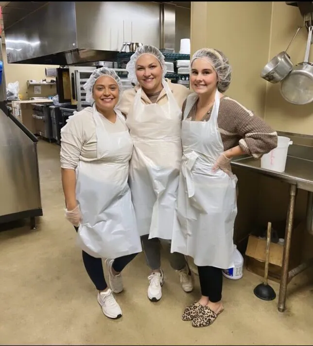 Three Scott Pryor Law Group team members in aprons and hairnets volunteering in the Atlanta Mission kitchen