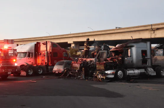 Firefighters at the burned wreckage of two tractor-trailers under a highway overpass