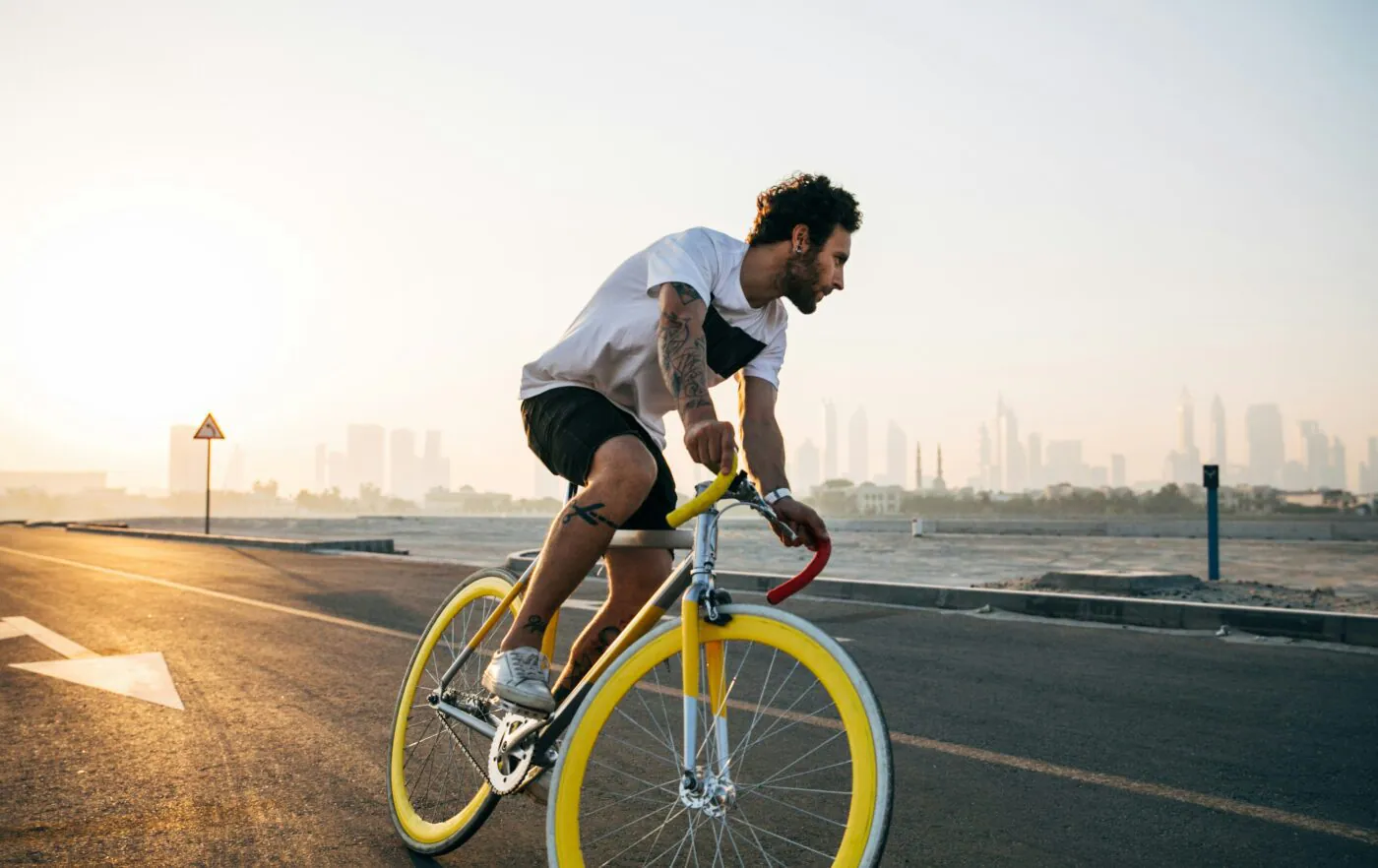 A cyclist riding a fixed-gear bike along a city road at sunrise