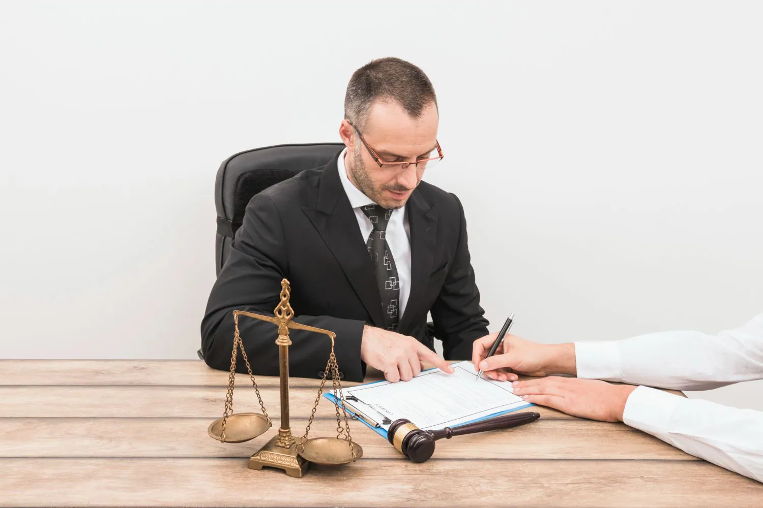 A lawyer at a desk with a scale and gavel as a client signs a document