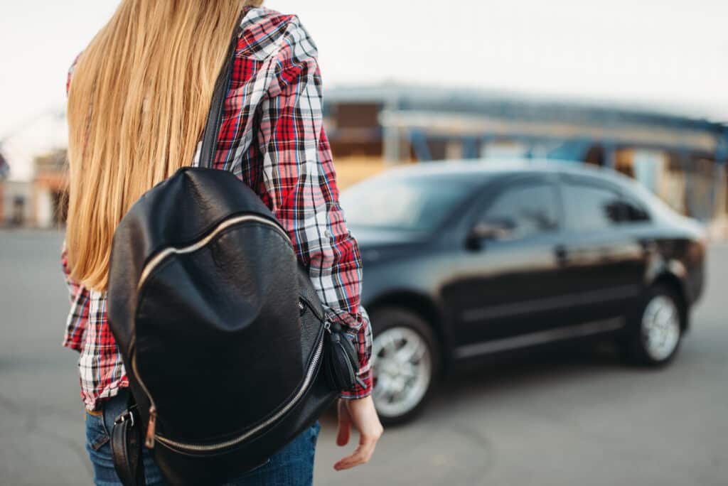 Young woman driver with bag against a car